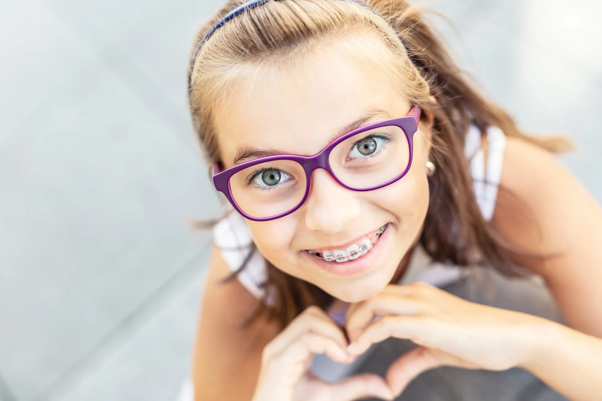 Smiling girl with braces and purple glasses making a heart with her hands