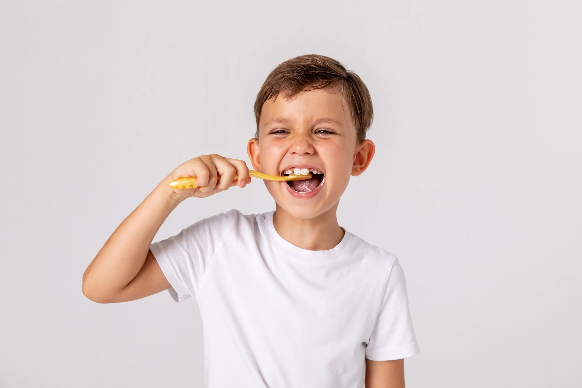 Smiling boy brushing his teeth with a yellow toothbrush