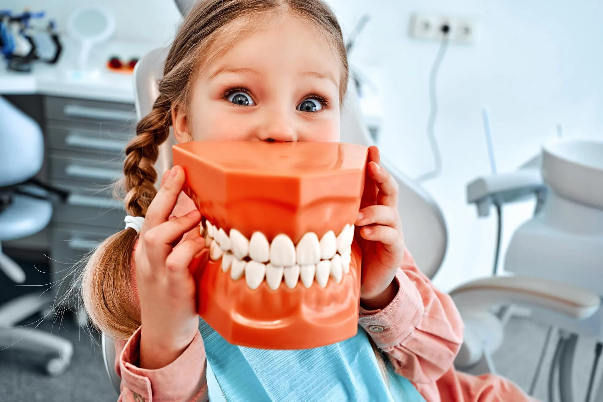 Little girl holding a giant model of teeth in a dental office